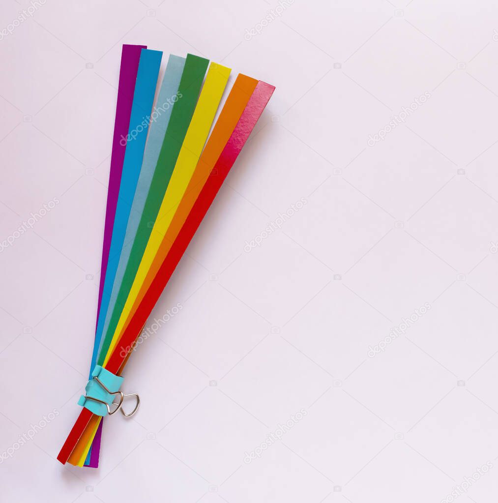 Rainbow bouquet. Strips of rainbow colored paper are held together with a paper clip. Light pink background. 