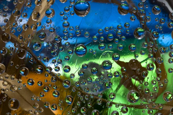 Transparent drops of water flow down on a multi-colored background with dry leaves located on it. Abstract fantasy. 3D render.