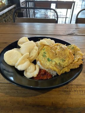 Pirinçli omlet ve küçük krakerler ahşap bir restoran masasında siyah bir tabakta servis ediliyor.