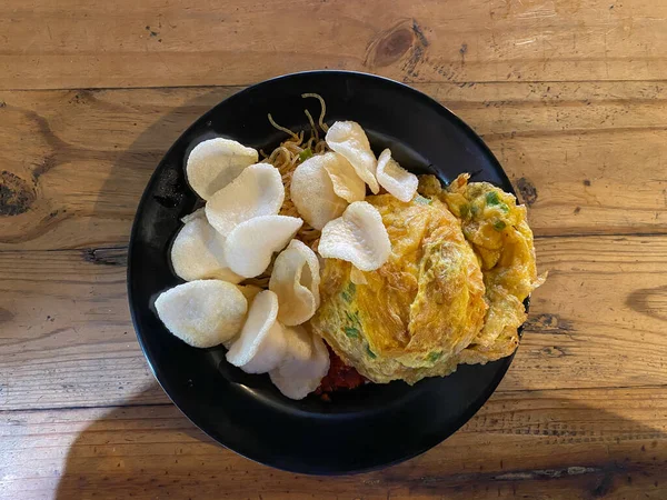 Pirinçli omlet ve küçük krakerler ahşap bir restoran masasında siyah bir tabakta servis ediliyor.