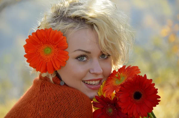 Piękna kobieta portret odkryty na słoneczny dzień i czerwone kwiaty — Zdjęcie stockowe