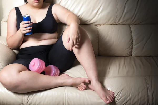 Mujer gorda cansada renunciar a concepto de ejercicio y refresco en la mano gota mancuerna sentado en el sofá —  Fotos de Stock