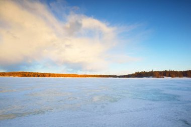 Gün batımında donmuş göl ve karla kaplı çam ormanı. Buz dokusu. Dramatik gökyüzü, yumuşak güneş ışığı. Idyllic kış sahnesi. Doğa, çevre koruma, ekoloji, iklim değişikliği, eko-turizm, Noel