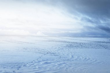 Gün batımında kar fırtınasından sonra karla kaplı arazinin panoramik görüntüsü. Taze karda insan izleri. Buz çölü. Dramatik bulut manzarası. Küresel ısınma teması. Laponya, Finlandiya