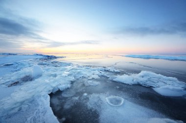 Gün batımında donmuş Saima gölünün karla kaplı kıyılarının panoramik görüntüsü. Buz parçaları yakın plan. Renkli bulutlu bir manzara. Suyun simetri yansımaları. Finlandiya