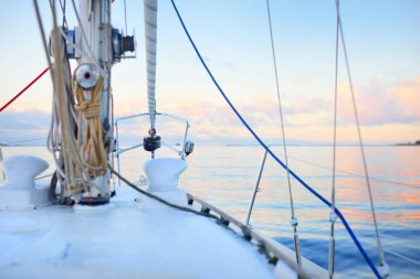 Gün batımında durgun suda yüzen beyaz bir yat. Buz ve güvertedeki ilk kar, pruvaya, direğe, halatlara ve yelkenlere yakın görüş. Renkli kış bulutlarıyla açık mavi gökyüzü. Norveç