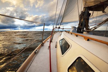 Gün batımında açık denizde yelken açmak. Güverteden pruvaya, direğe ve yelkenlere yakın görüntü. Dramatik fırtınalı gökyüzü, kara bulutlar, kış kasırgası, sert hava. Destansı deniz manzarası. Kuzey denizi, Norveç
