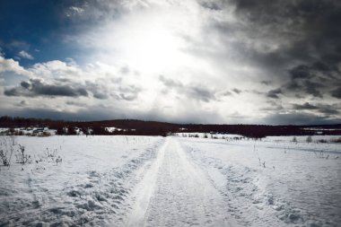 Kar fırtınasından sonra karla kaplı arazide keskin bir dönüş yapan boş bir köy yolu. Parlak bulutlu dramatik bir gökyüzü. Karelia, Rusya. Yol gezisi, eko turizm, çevre koruma kavramları