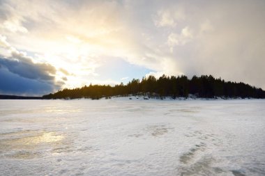Gün batımında donmuş göl ve çam ormanı. Buz dokusu. Dramatik fırtınalı mavi gökyüzü, destansı bulutlar. Kış Harikalar Diyarı. Doğa, ekoloji, iklim değişikliği, eko-turizm, kararsız hava