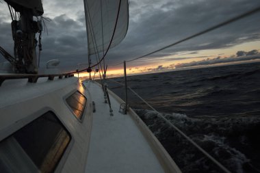 Gün batımında açık denizde yelken açmak. Güverteden pruvaya, direğe ve yelkenlere yakın görüntü. Dramatik fırtınalı gökyüzü, kara bulutlar, kış kasırgası, sert hava. Destansı deniz manzarası. Kuzey denizi, Norveç
