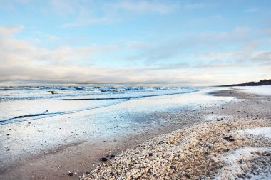 Bir sürü deniz kabuğuyla kaplı Baltık deniz kıyısından bir manzara. Riga Körfezi, Letonya. Renkli dramatik bulut manzarası. Kararsız hava, dalgalar, su sıçramaları. Kış turizmi, küresel ısınma