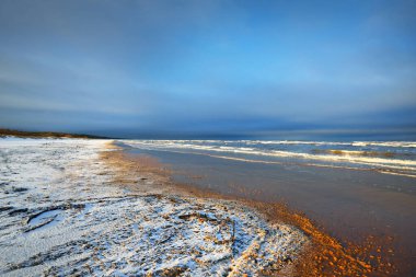 Gün batımında karla kaplı Baltık deniz kıyısından bir manzara. Riga Körfezi, Letonya. Dramatik mavi gökyüzü. Kararsız hava, dalgalar ve su sıçramaları. Kış turizmi, küresel ısınma teması