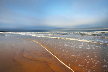 Gün batımında karla kaplı Baltık deniz kıyısından bir manzara. Riga Körfezi, Letonya. Dramatik mavi gökyüzü. Kararsız hava, dalgalar ve su sıçramaları. Kış turizmi, küresel ısınma teması