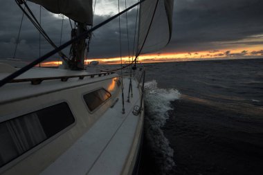 Bir kış günü açık denizde yat gezintisi. Güverteden pruvaya, direğe ve yelkenlere yakın görüntü. Dramatik fırtınalı gökyüzü, kara bulutlar. Destansı deniz manzarası. Kuzey denizi, Norveç
