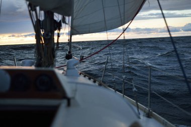 Bir kış günü açık denizde yat gezintisi. Güverteden pruvaya, direğe ve yelkenlere yakın görüntü. Dramatik fırtınalı gökyüzü, kara bulutlar. Destansı deniz manzarası. Kuzey denizi, Norveç
