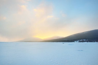 Gün batımında donmuş bir göl kıyısında buz basıncı sırtı. Arka planda dağ zirveleri var. Renkli bulutlu bir manzara. Resimli kış manzarası. Ekoloji, çevre, iklim değişikliği, küresel ısınma kavramları
