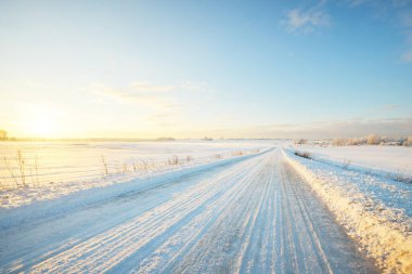 Gün batımında kar fırtınasından sonra karla kaplı arazide köy yolu. Gökyüzü açık, altın ışık. Idyllic kırsal kesim. Panoramik manzara. Noel, lojistik, tehlikeli sürüş, off-road, ulaşım