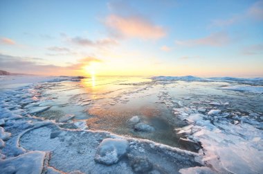 Gün batımında donmuş Saima gölünün karla kaplı kıyılarının panoramik görüntüsü. Buz parçaları yakın plan. Renkli bulutlu bir manzara. Suyun simetri yansımaları. Finlandiya