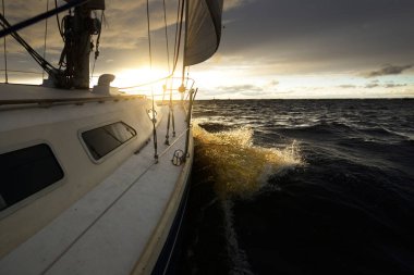 Bir kış günü açık denizde yat gezintisi. Güverteden pruvaya, direğe ve yelkenlere yakın görüntü. Dramatik fırtınalı gökyüzü, kara bulutlar. Destansı deniz manzarası. Kuzey denizi, Norveç
