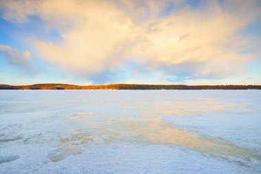 Gün batımında donmuş göl ve karla kaplı çam ormanı. Buz dokusu. Dramatik gökyüzü, yumuşak güneş ışığı. Idyllic kış sahnesi. Doğa, çevre koruma, ekoloji, iklim değişikliği, eko-turizm, Noel