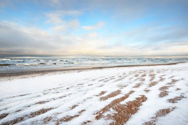 Gün batımında karla kaplı Baltık deniz kıyısından bir manzara. Riga Körfezi, Letonya. Renkli dramatik bulut manzarası. Kararsız hava, dalgalar ve su sıçramaları. Kış turizmi, küresel ısınma teması