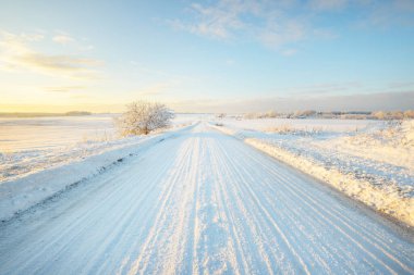 Gün batımında kar fırtınasından sonra karla kaplı arazide köy yolu. Gökyüzü açık, altın ışık. Idyllic kırsal kesim. Panoramik manzara. Noel, lojistik, tehlikeli sürüş, off-road, ulaşım