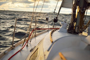 Gün batımında bir kış günü açık denizde yelken açmak. Güverteden pruvaya, direğe ve yelkenlere yakın görüntü. Dramatik gökyüzü, kara bulutların arasından geçen altın güneş ışığı. Destansı deniz manzarası. Kuzey denizi, Norveç
