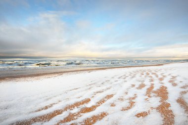 Gün batımında karla kaplı Baltık deniz kıyısından bir manzara. Riga Körfezi, Letonya. Renkli dramatik bulut manzarası. Kararsız hava, dalgalar ve su sıçramaları. Kış turizmi, küresel ısınma teması
