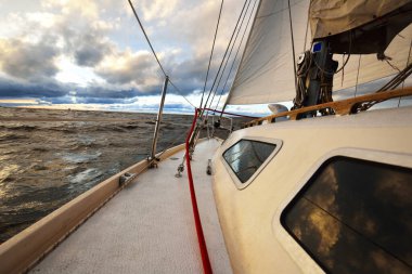 Gün batımında bir kış günü açık denizde yelken açmak. Güverteden pruvaya, direğe ve yelkenlere yakın görüntü. Dramatik gökyüzü, kara bulutların arasından geçen altın güneş ışığı. Destansı deniz manzarası. Kuzey denizi, Norveç