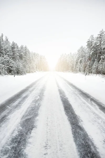 Snow-covered highway (asphalt road) through the coniferous forest after a blizzard. Lapland, Finland. Dangerous driving, climate change, global warming, ecology, environmental conservation