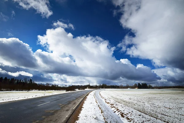 吹雪の後 雪に覆われた国の道路や農業分野の上に積雲と劇的な青い空 ラトビアの冬 壮大な雲の風景 気候変動 地球温暖化のテーマ — ストック写真