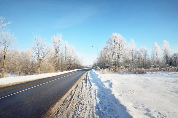 清理后的一条空旷的沥青路面 街灯特写特写 新雪中的车辙 后面是白雪覆盖的桦树林 晴朗的蓝天 芬兰的冬季驾驶 全球变暖主题 — 图库照片