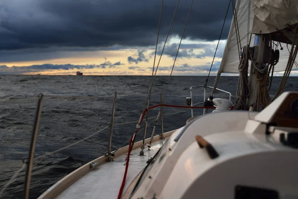 Yacht sailing in an open sea on a winter day. Close-up view from the deck to the bow, mast and sails. Dramatic stormy sky, dark clouds. Epic seascape. North sea, Norway