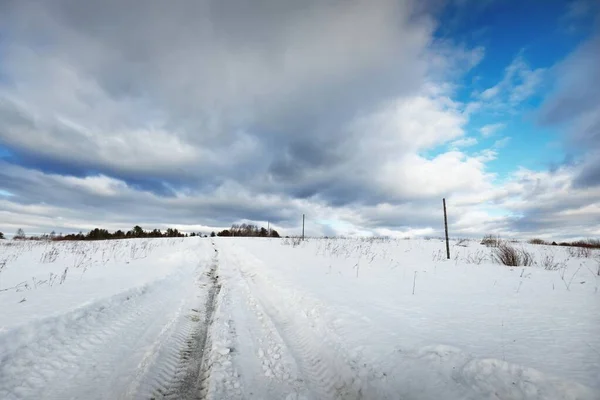 吹雪の後に雪に覆われたフィールドを空の道路 輝く雲と劇的な空 冬の田園風景 旅行先 エコツーリズム オフロード 遠隔村 — ストック写真