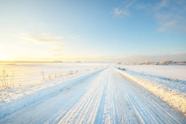 夕暮れ時の吹雪の後に雪に覆われたフィールドを介して田舎道 澄んだ空黄金の光 牧歌的な田園風景 パノラマビュー クリスマス 危険な運転 オフロード — ストック写真