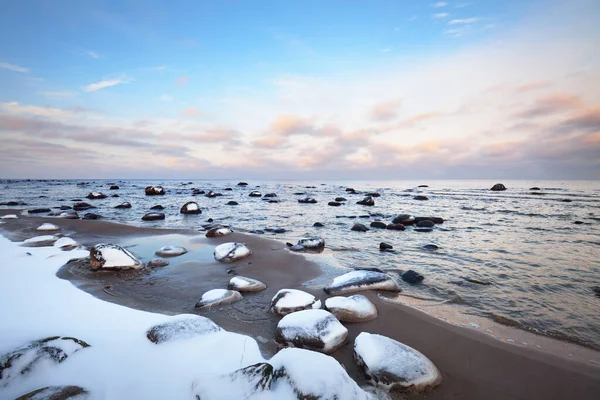 日没の雪に覆われたバルト海沿岸の景色 水の中の石を閉じる カラフルな雲と澄んだ青い空 見事な雲景だ 暖かい夜の光 牧歌的な冬のシーン ラトビアのカルテネ — ストック写真