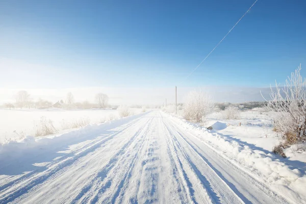 晴れた日にフィールドを介して雪に覆われたシングルレーン農村道路 フィンランドだ 真っ青な空 背景の霜の落葉樹と常緑樹 牧歌的な冬の風景 — ストック写真