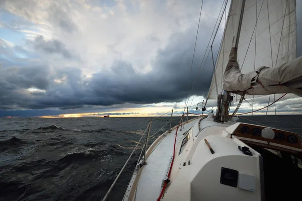 Yacht sailing in an open sea on a winter day. Close-up view from the deck to the bow, mast and sails. Dramatic stormy sky, dark clouds. Epic seascape. North sea, Norway