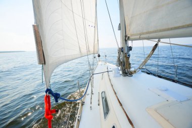 Güneşli bir yaz gününde beyaz bir yat denize açılıyor. Güverteden pruva ve yelkenlere kadar yukarıdan aşağıya doğru. Dalgalar ve su sıçramaları. Açık mavi gökyüzü. Baltık Denizi, İsveç