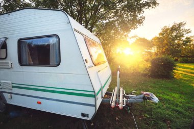 Karavan, gün batımında ağaçların altındaki yeşil çimlere park etmiş. Brittany, Fransa. Tatiller, boş zaman aktiviteleri, eğlence, turizm, yol gezisi, seyahat yerleri, yaşam tarzı
