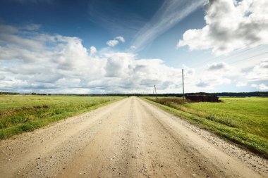 Yağmurdan sonra tarlalardan geçen boş bir köy yolu. Dramatik gökyüzü, destansı bulutlar. Hava kararsız. Transformatör direkleri yakın çekim. Letonya