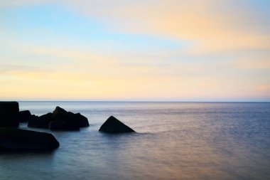 Renkli günbatımı gökyüzüne karşı dalgalı su. Göz kamaştırıcı deniz manzarası. Mavi bulutların arasından geçen altın gün batımı ışığı. Uzun pozlama. Baltık Denizi, Riga Körfezi, Letonya