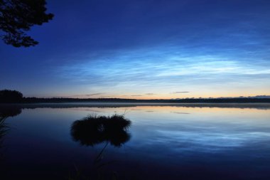 Yaz gündönümü gecesinde Saimaa Gölü 'nün üzerinde gece parlayan bulutlar ve sis vardı. Altın güneş ışığı. Uzun pozlama. Destansı bulut manzarası. Doğal desen. Suyun simetri yansımaları. Finlandiya