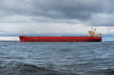 Büyük kırmızı kargo gemisi karanlık günbatımı göğünün altında açık denizde yol alıyor. Southampton 'da. İngiltere. Dramatik bulutlar, kasırga, fırtınalı hava. Küresel iletişim, nakliye, endüstri, lojistik