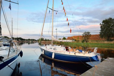 Zarif ve modern yelkenli tekneler (kiralık) açık bir günde yat limanındaki bir rıhtıma demirlediler. Ulaşım, spor ve eğlence teması. İsveç. Mavi yelkenli donanımlı yelkenli. Yakın plan.