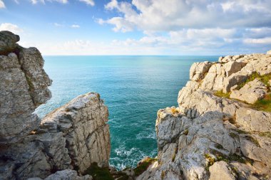 Pointe de Pen-Hir 'in kayalık sahili, uçurumlara yakın. Bulutlu mavi gökyüzü, masmavi su, fırtınalı dalgalar. Dramatik bulut manzarası. Crozon Yarımadası, Britanya, Fransa