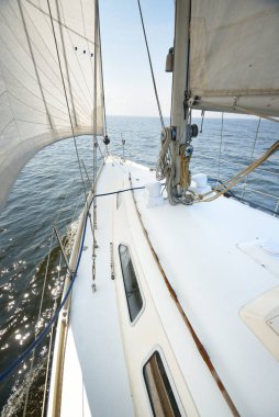 Güneşli bir yaz gününde beyaz bir yat denize açılıyor. Güverteden pruva ve yelkenlere kadar yukarıdan aşağıya doğru. Dalgalar ve su sıçramaları. Açık mavi gökyüzü. Baltık Denizi, İsveç
