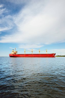 Europoort 'tan denize açılan bir vinçle büyük kırmızı bir yük gemisi (kargo gemisi). Açık mavi gökyüzü ve sirrus bulutları. Rotterdam, Hollanda. Küresel iletişim, lojistik, endüstri teması