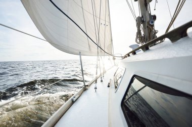 Güneşli bir yaz gününde açık denizde yelken açan beyaz bir yat. Güverteden pruva ve yelkenlere kadar yakın çekim. Dalgalar ve su sıçramaları. Sirus bulutları ve uçak izleri olan açık mavi bir gökyüzü. Hollanda