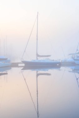 Yelkenli tekneler, güneşin doğuşunda yoğun beyaz bir sisle bir rıhtıma demirlediler. Kiel, Almanya 'daki yat kulübü. Spor, eğlence, ulaşım teması